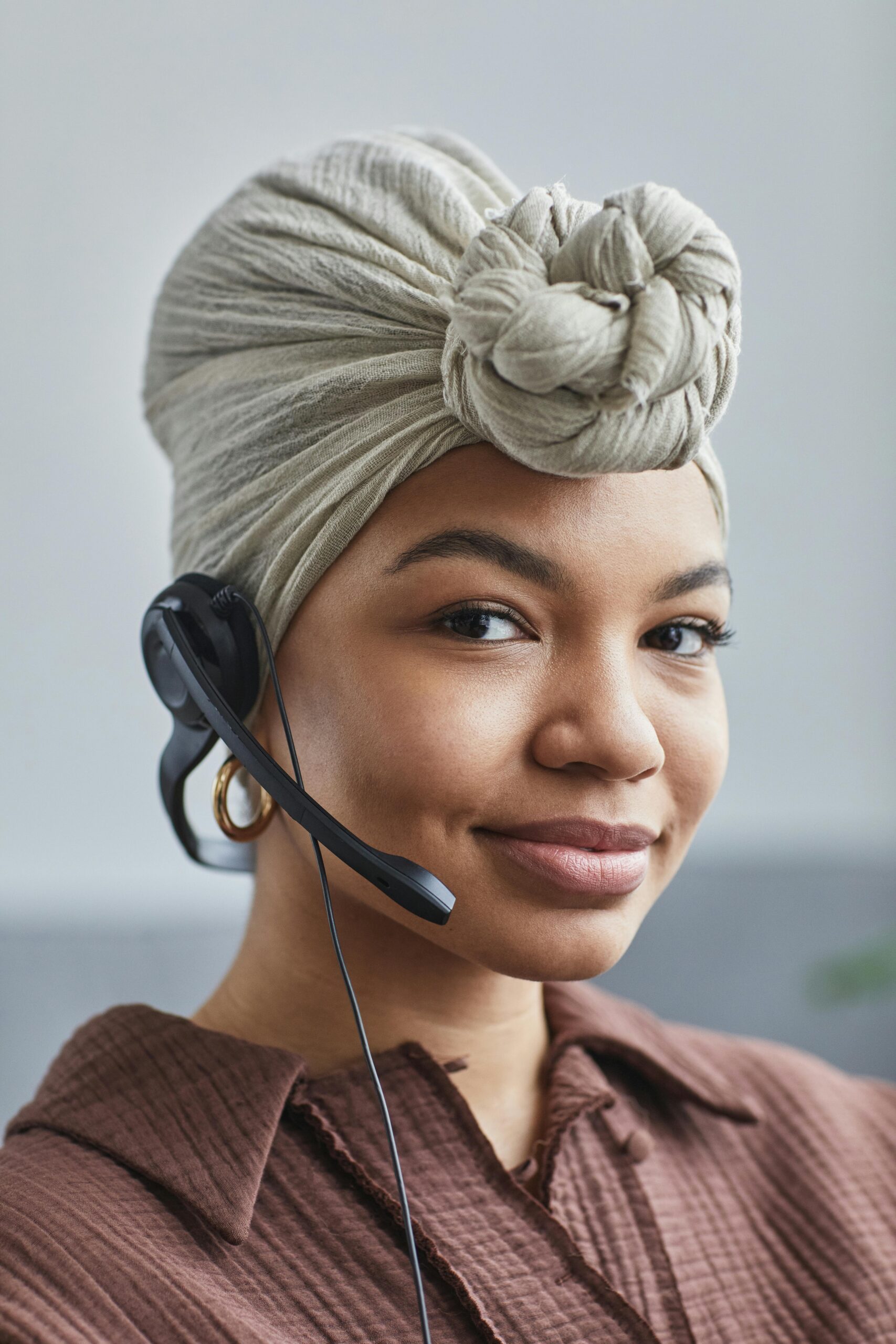 Smiling black woman in a head wrap and headset working in a call center.