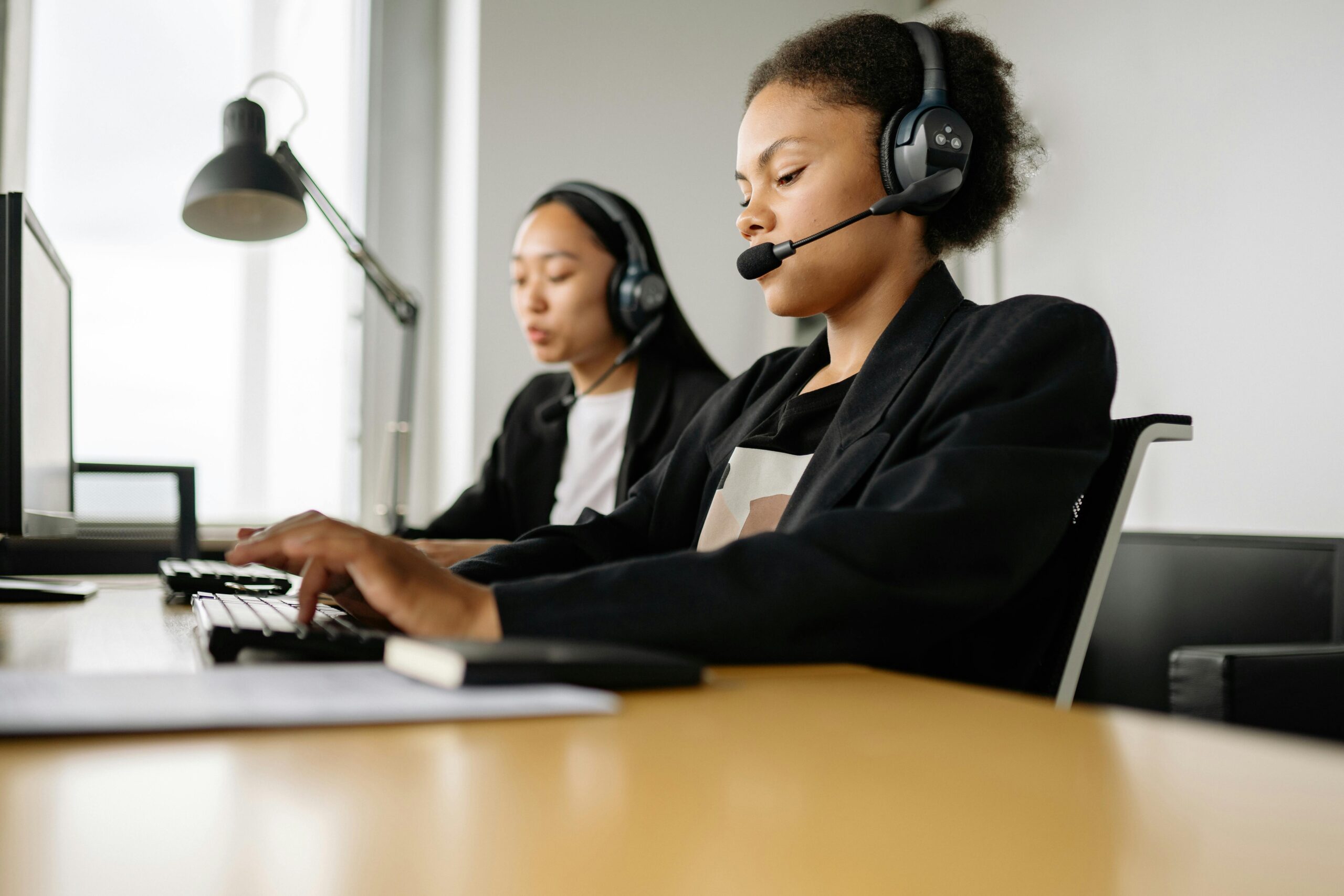Two call center agents working at desks in an office setting with headsets.